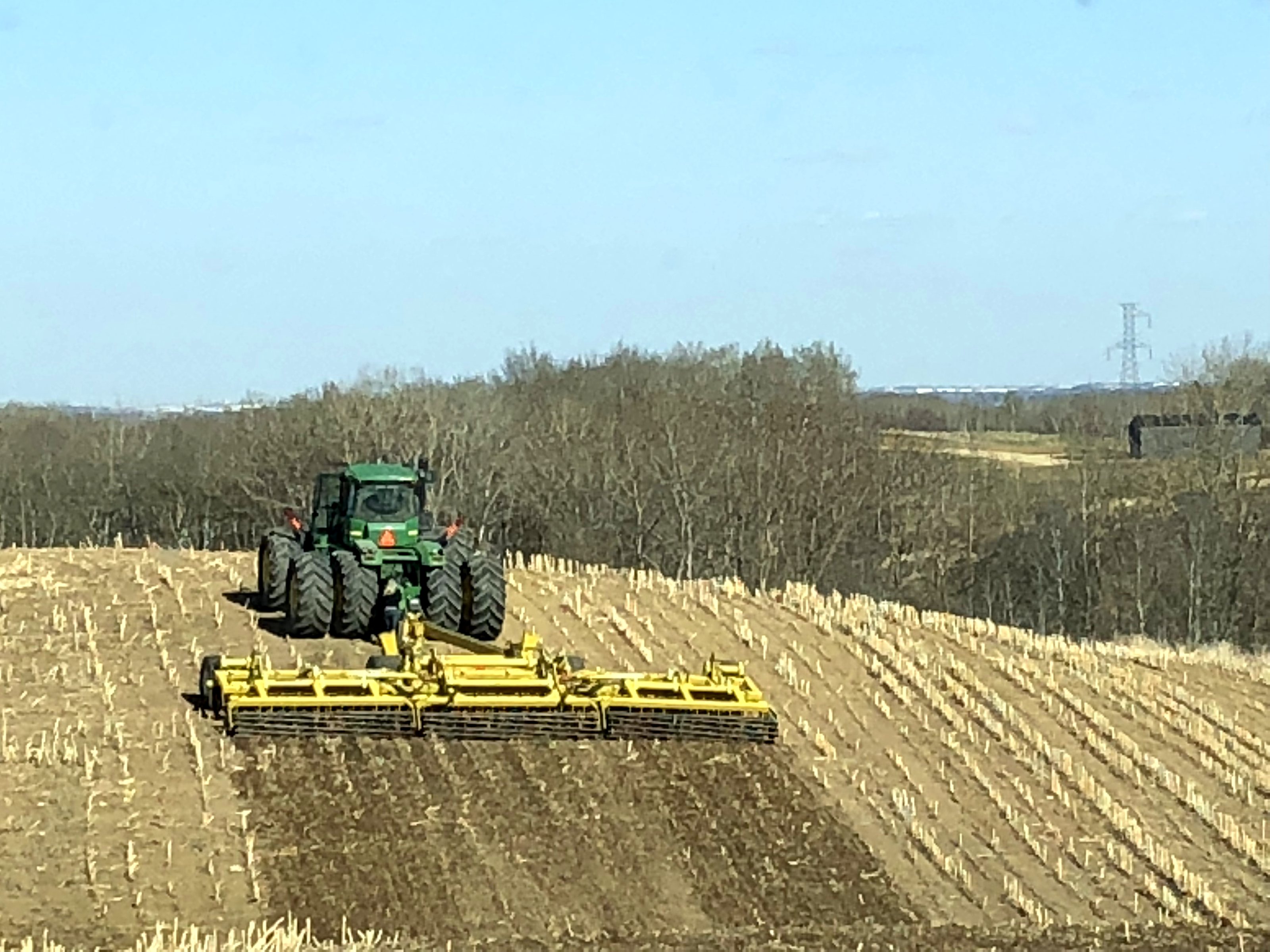 A John Deere tractor pulling a Degelman Pro-Till high-speed disc across stubble in spring